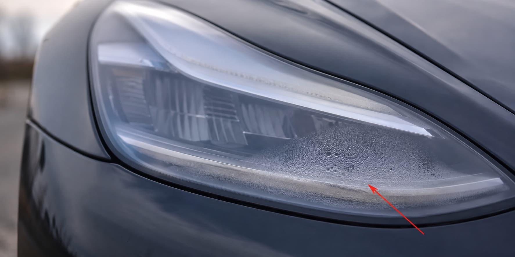 Condensação dentro da lanterna de um Tesla Model Y, marcada com uma seta vermelha