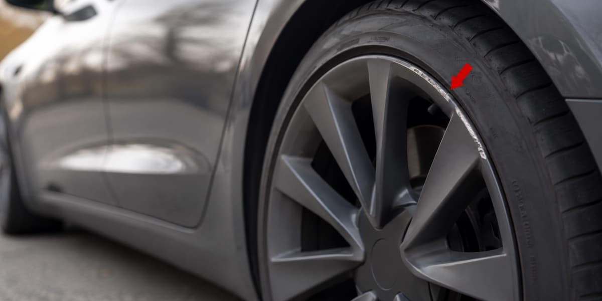 Curb rash damage on a Tesla wheel rim, marked with a red arrow